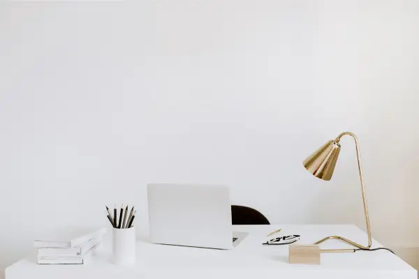 Foto de um notebook sobre uma mesa com uma luminária e um porta lápis em um espaço clean